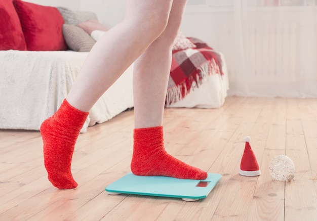 Pies femeninos de pie sobre balanzas electrónicas azules para control de peso en calcetines rojos con decoración navideña