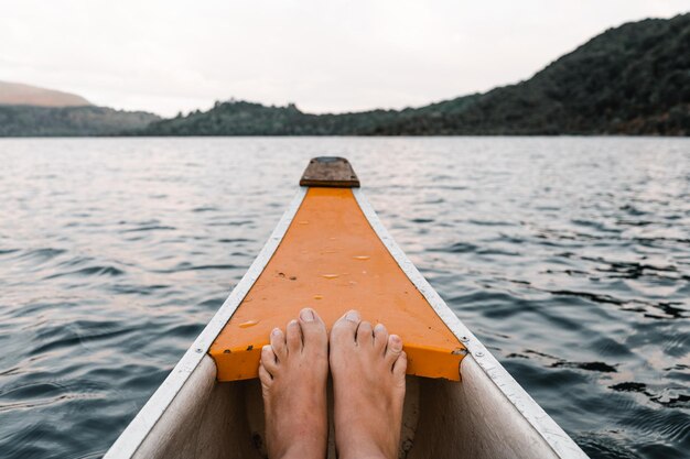 Los pies juntos dentro de una canoa de madera naranja y blanca navegando hacia las montañas de la orilla del lago