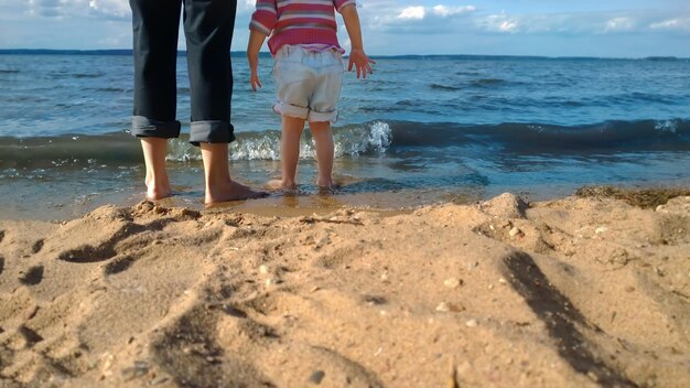 Los pies de una madre y un niño se paran en la arena junto a la orilla del mar