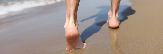 Pies masculinos caminando sobre la arena en la playa closeup