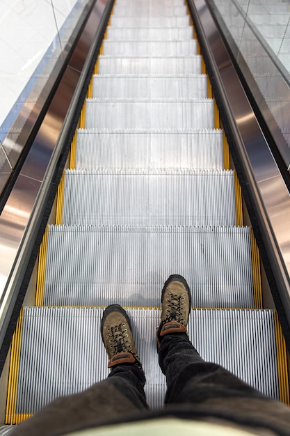 Pies masculinos en la escalera mecánica, vista superior.