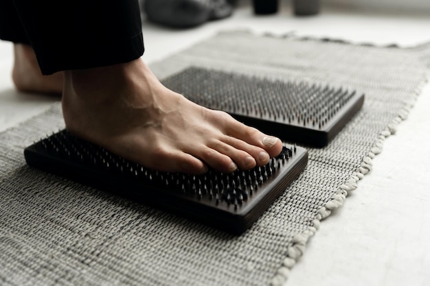 Pies masculinos jóvenes parados sobre una tabla con clavos sobre un fondo blanco. tablero de sadhu. yoga matutino. búsqueda zen