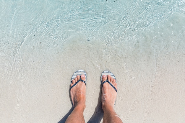 Pies masculinos vistiendo chanclas femeninas en la playa