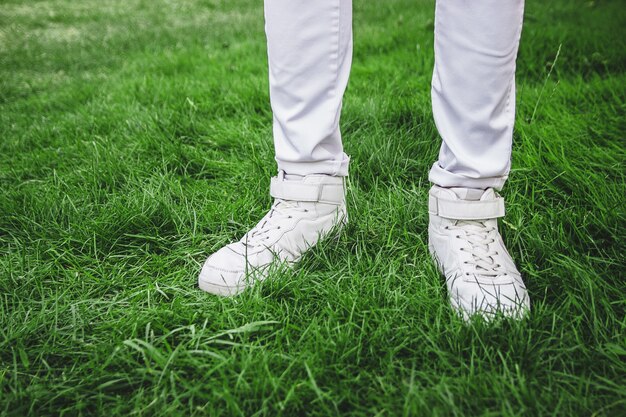 Pies masculinos con zapatos blancos sobre la hierba verde. Jeans blancos.