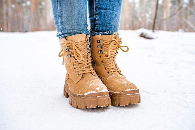 Pies de mujer con botas amarillas en la nieve en un bosque nevado