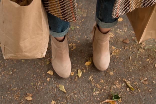 Pies de mujer en botas con bolsas en otoño al aire libre