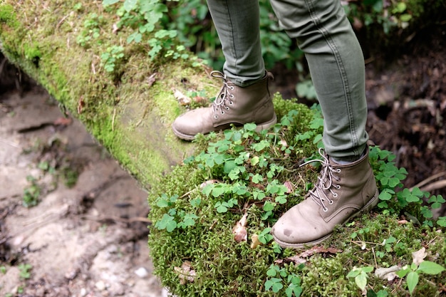 Los pies de la mujer en botas de viaje en un tronco cubierto de musgo en el bosque. Concepto de viaje.