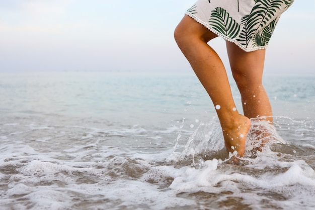 Los pies de la mujer caminan lentamente y se relajan en la arena de la playa tropical con fondo de cielo azul. Concepto de vacaciones y vacaciones.