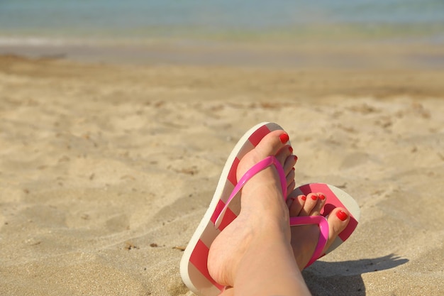 Pies de mujer con chanclas en la arena