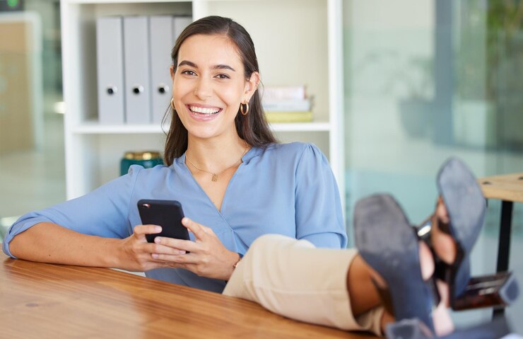 Foto pies de mujer y escritorio en retrato con sonrisa de teléfono inteligente y aplicación de redes sociales en el lugar de trabajo oficina de líder ejecutivo feliz y teléfono inteligente para comunicación en red o red social en los ángeles