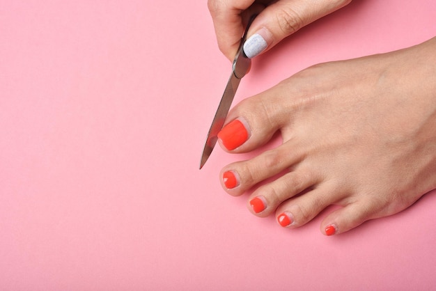 Pies de mujer sobre fondo rosa, pedicura de uñas rojas, concepto de salón de belleza.