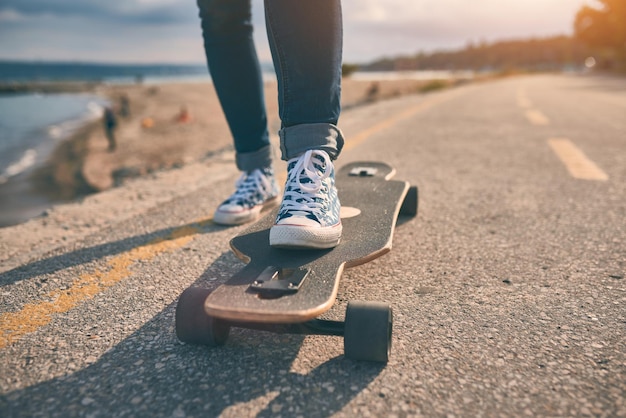 Pies de mujer en zapatillas de deporte en un longboard en la noche