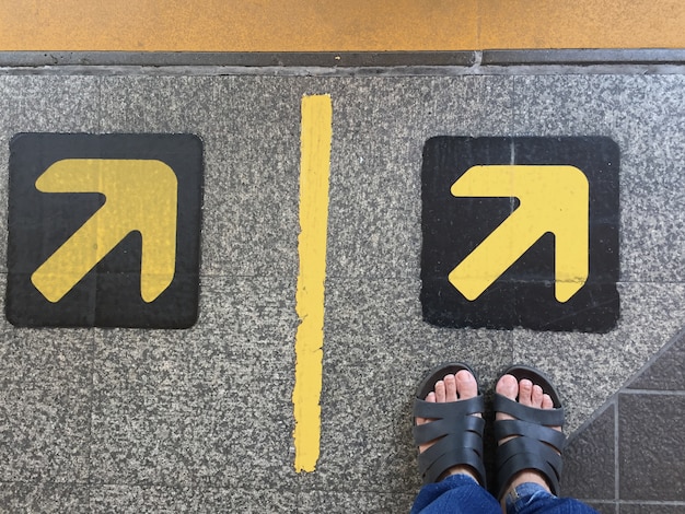 pies de mujeres en la sandalia de pie en el signo de la flecha en la estación de BTS