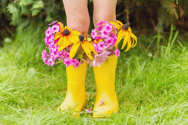 Pies de niño en botas de goma amarillo con flores de otoño.