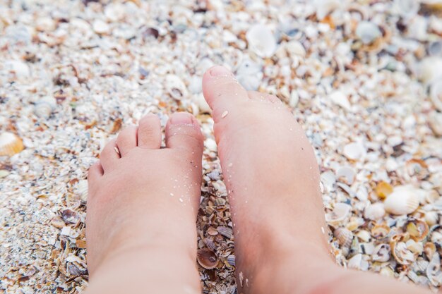 Los pies de los niños están de pie en la playa sobre la arena amarilla soleada