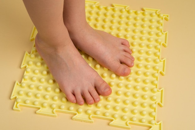 Pies de niños sobre una alfombra ortopédica amarilla sobre un fondo beige tratamiento y prevención de pies planos hallux valgus un lugar para texto