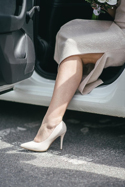 los pies de la novia con zapatos de boda blancos saliendo del auto