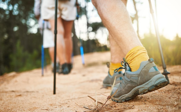 Pies o zapatos caminando y caminando por un sendero que sube una montaña con palos y bastones Primer plano de un grupo de excursionistas aventureros o amigos que exploran un camino accidentado en una montaña en la naturaleza