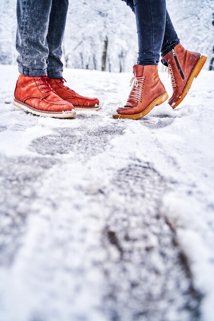 Pies de una pareja en una acera nevada con botas marrones