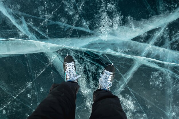 Pies en patines en el hermoso hielo azul agrietado de un lago congelado Vista de la parte superior