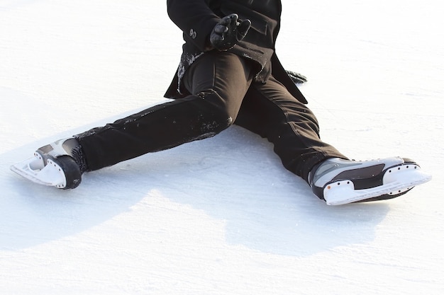 Pies en patines de un hombre caído en una pista de hielo