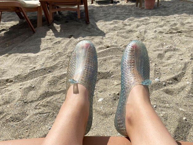 Pies de piernas femeninas en zapatillas de goma con una hermosa pedicura roja en el fondo de la arena