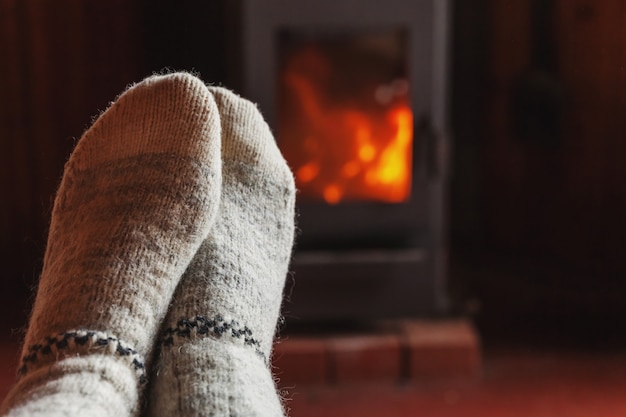 Pies piernas en ropa de invierno calcetines de lana en la chimenea en casa en invierno u otoño por la noche relajándose y calentándose