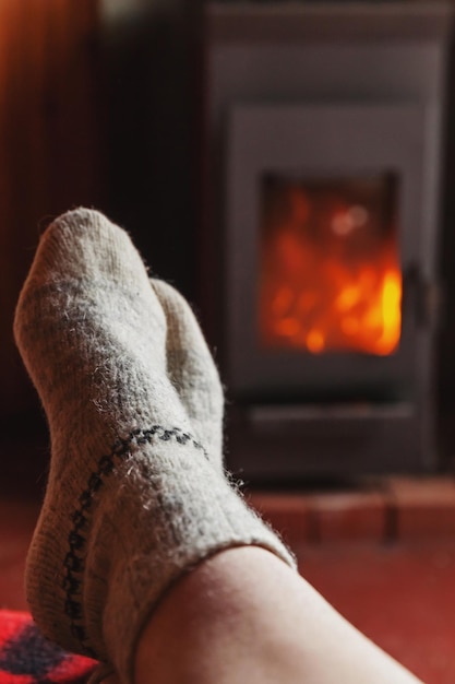 Pies piernas en ropa de invierno calcetines de lana en el fondo de la chimenea mujer sentada en casa en invierno o au ...
