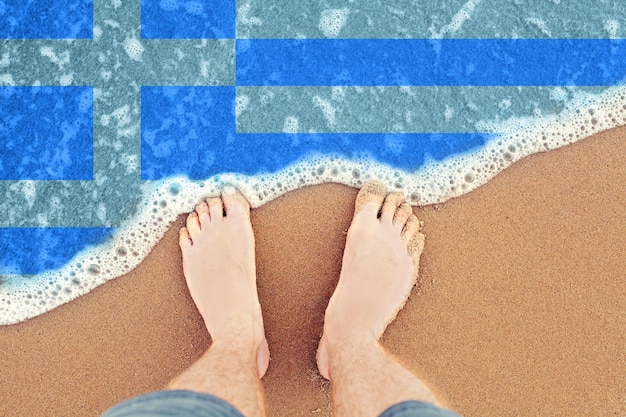 Pies en la playa de arena con bandera Grecia Vista superior sobre la ola del mar