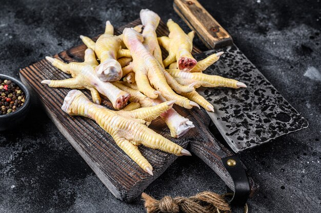 Pies de pollo crudo sobre tabla de cortar de carnicero con cuchilla