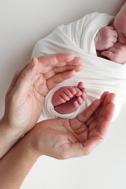 Pies del recién nacido en las palmas de los padres Fotografía de estudio de los dedos de los pies de un niño, talones y pies Las palmas del padre, la madre, sostienen el pie del bebé recién nacido en una manta blanca