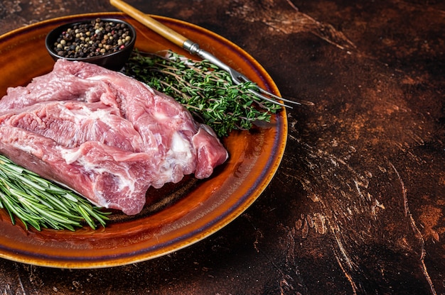 Pieza cruda de carne de paleta de cerdo con especias en un plato rústico.