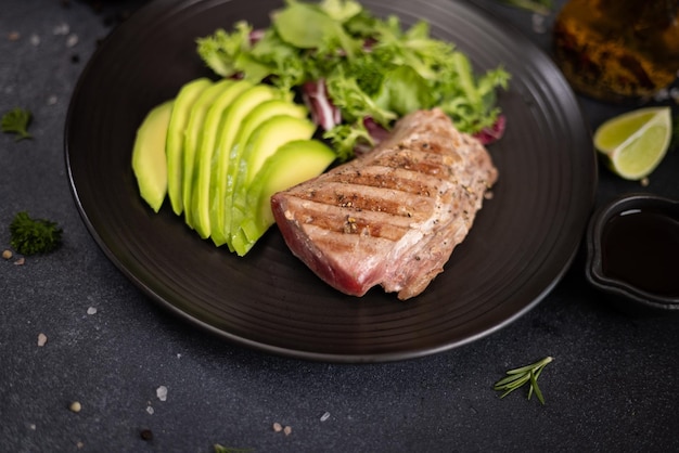 Pieza de filete de atún cocido a la parrilla con aguacate cortado y ensalada en una placa de cerámica negra