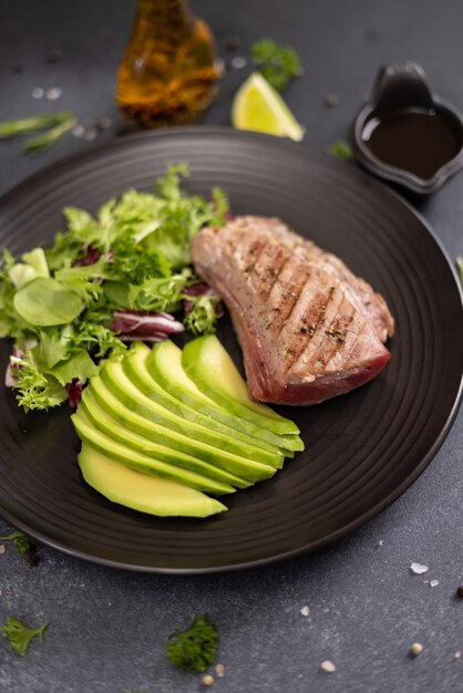 Pieza de filete de atún cocido a la parrilla con aguacate cortado y ensalada en una placa de cerámica negra