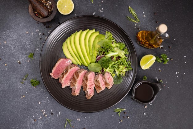 Pieza de filete de atún cocido a la parrilla con aguacate cortado y ensalada en una placa de cerámica negra