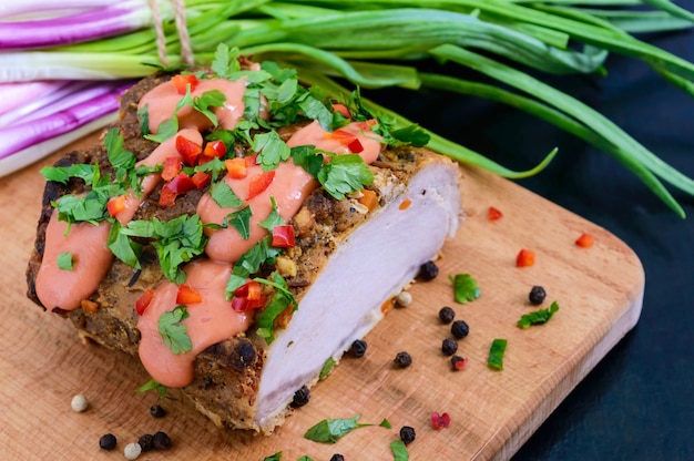 Pieza grande de jamón de cerdo al horno, con cebollas verdes y salsa en la tabla de cortar