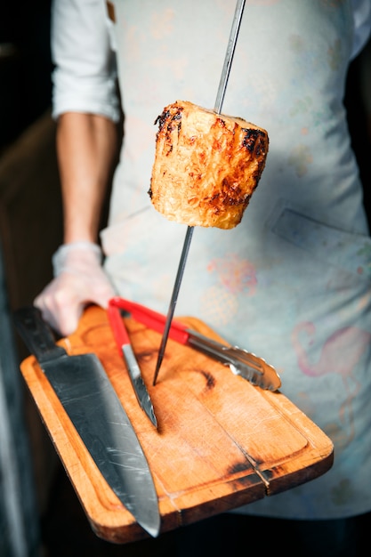 Una pieza, piña drapeada, está en la brocheta. El chef sostiene a un cocinero con guantes blancos. Pincho descansa sobre una tabla de cortar de madera.