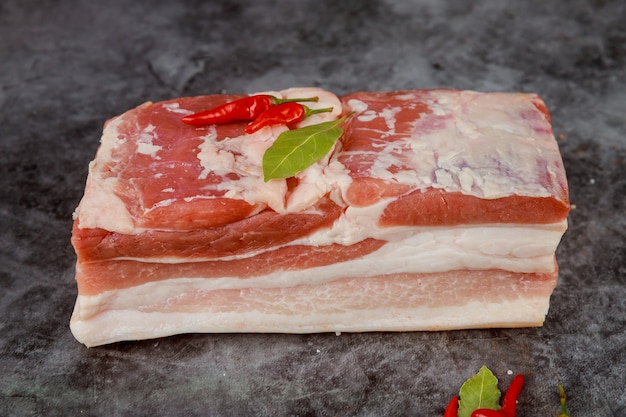 Pieza roja y blanca de panceta de cerdo cruda con ajo y especias sobre fondo oscuro.