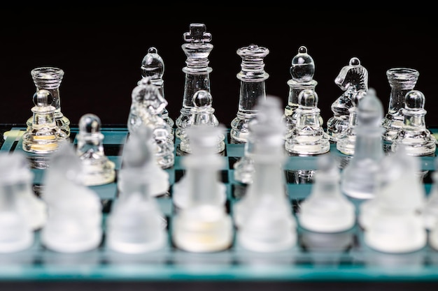 Piezas de ajedrez transparentes de vidrio en un primer plano de enfoque selectivo de tablero de ajedrez aislado en negro