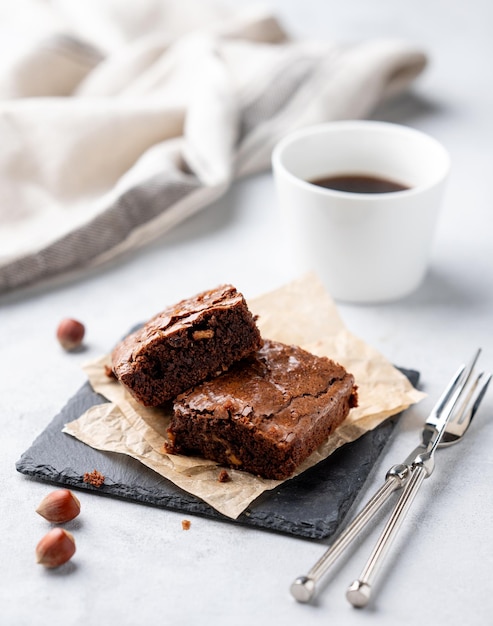 Piezas de brownies de chocolate con avellanas y caramelo salado en papel de hornear sobre un fondo claro con una taza de café