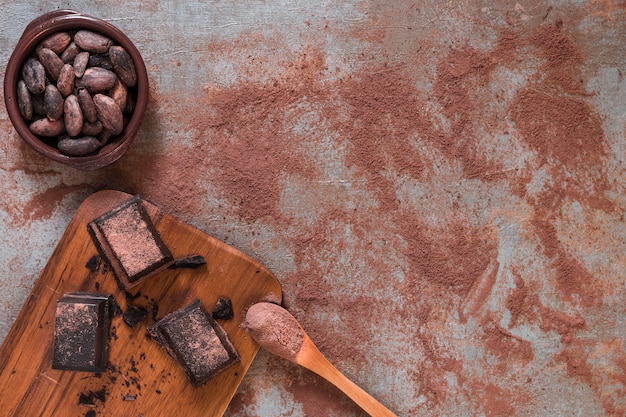 Piezas de chocolate en tajadera y tazón de granos de cacao