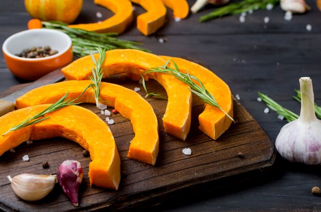 Piezas crudas de calabaza sobre una tabla de cortar con romero