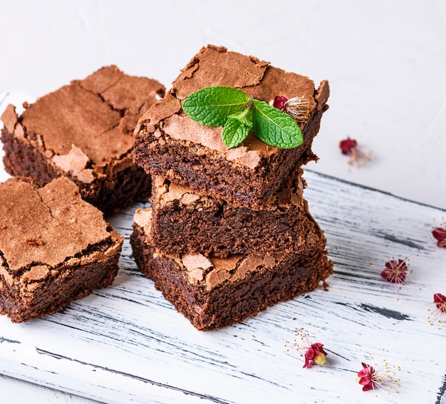 Piezas cuadradas de pastel de brownie al horno sobre una tabla de madera blanca