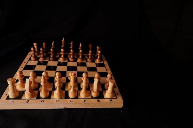 Piezas de madera blancas y negras sobre un tablero de ajedrez Un tablero de ajedrez colocado durante un juego sobre un fondo negro