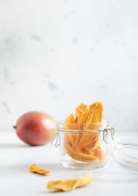 Piezas de mango seco en frasco de vidrio y fruta cruda sobre un fondo claro