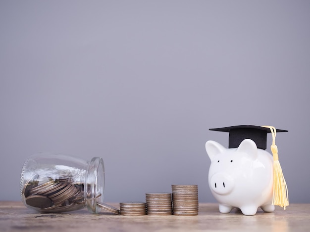 Piggy Bank mit Abschlussmütze und Münzstapel Das Konzept, Geld für Bildung zu sparen, Studentendarlehen, Stipendien, Studiengebühren in der Zukunft