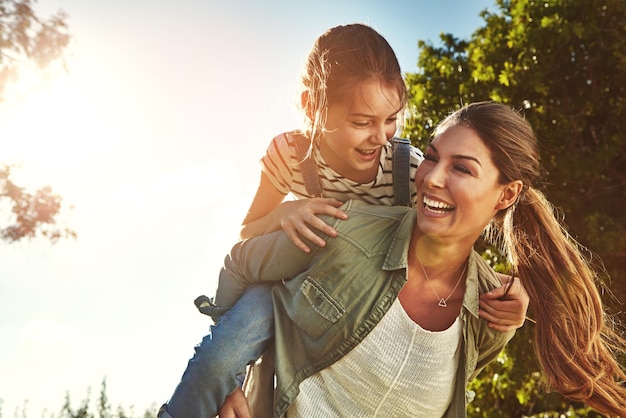 Piggyback feliz y una madre y un niño en la naturaleza para unir la felicidad y el amor en verano Riendo relajarse y una madre y una niña en un parque o jardín para jugar juntos y pasar un buen rato