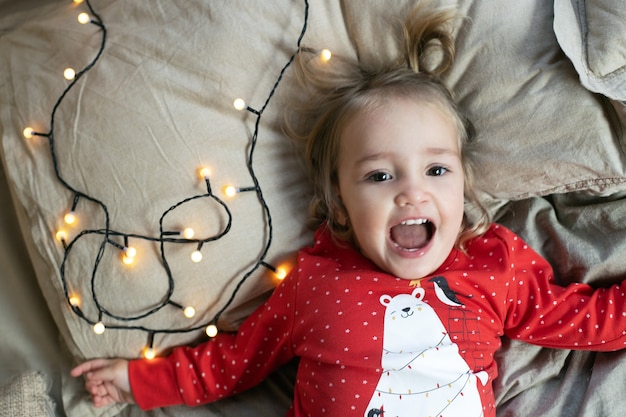 Pijama rojo de niña pequeña de la mañana de Navidad divirtiéndose en la cama