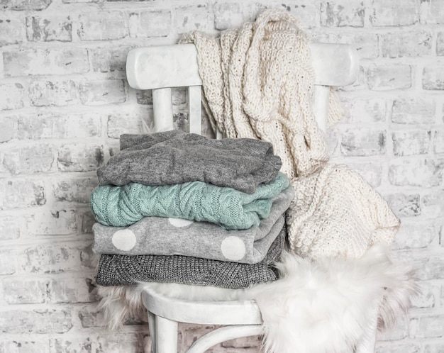 Pila de acogedores suéteres de otoño de invierno en una vieja silla blanca de madera en una habitación luminosa