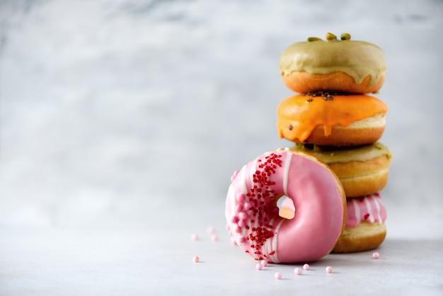 La pila de anillos de espuma clasificados coloridos esmaltados con asperja en fondo gris del cemento. Copia espacio Rosquillas dulces para niños.